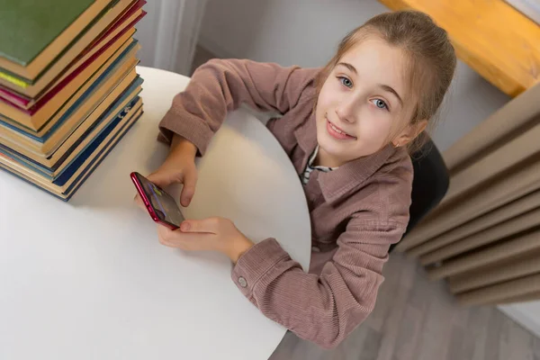 Девушка сидит за столом и смотрит на телефон — стоковое фото