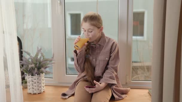 Dziewczyna pije sok z telefonem w rękach — Wideo stockowe