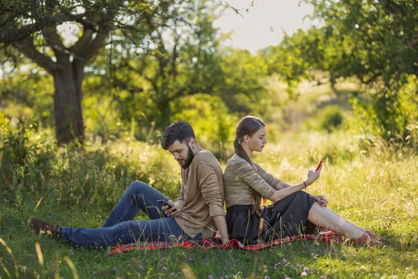 Paar zitten op het gazon en kijken naar hun telefoons — Stockfoto