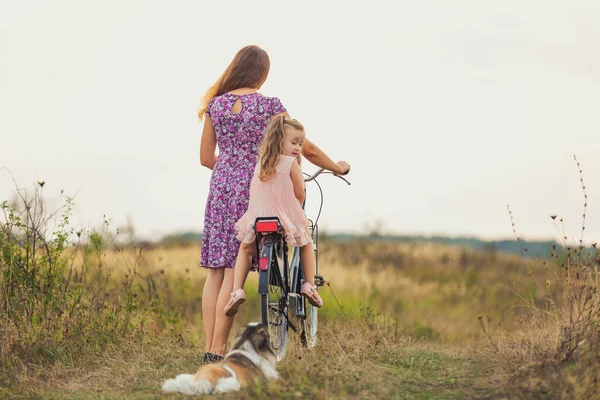 Mother and daughter walking with a bicycle and a dog — Stock Photo, Image