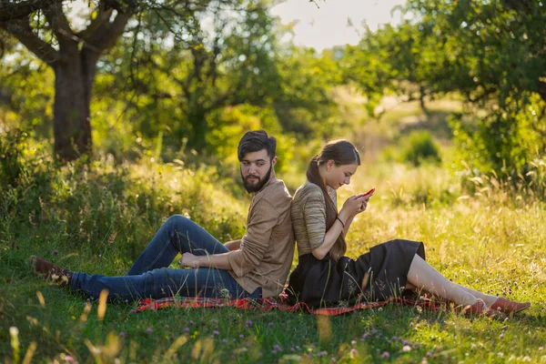 Pár ül a gyepen, és nézik a telefonjukat. — Stock Fotó