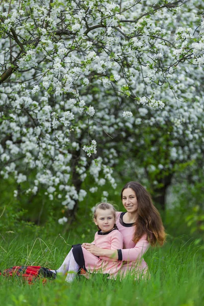Madre e hija sentadas en un huerto de manzanas — Foto de Stock