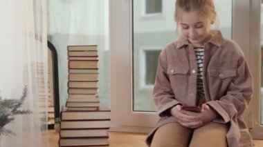 Kız pencere eşiğinde oturuyor ve telefona bakıyor.