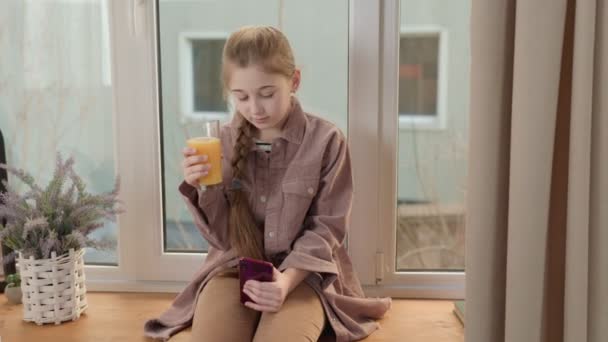 Девушка пьет сок с телефоном в руках — стоковое видео