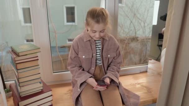 Dziewczyna siedzi na parapecie i patrzy na telefon — Wideo stockowe
