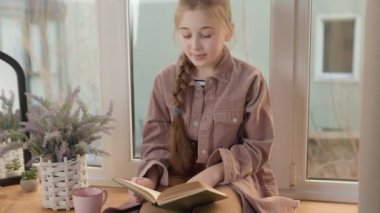 Kız pencerenin yakınındaki bir kitapla