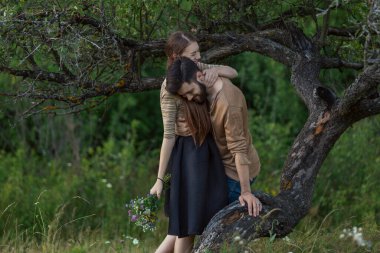 Bir ağacın yanında kucaklaşan çift.