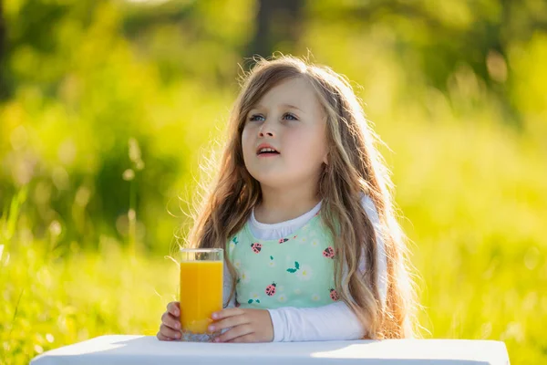 Child sits at a table on which there is a glass of juice — Stock Photo, Image