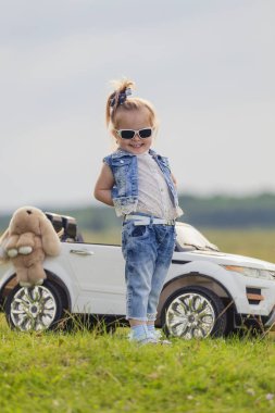 Güneş gözlüklü kız arabanın önünde duruyor.