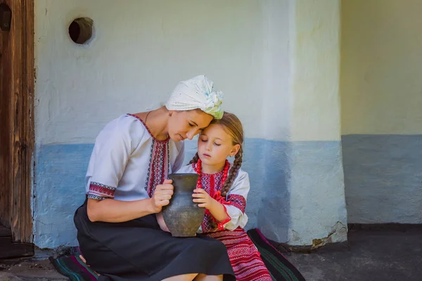 Mutter und Tochter in ukrainischen Trachten sitzen in der Nähe des Hauses — Stockfoto