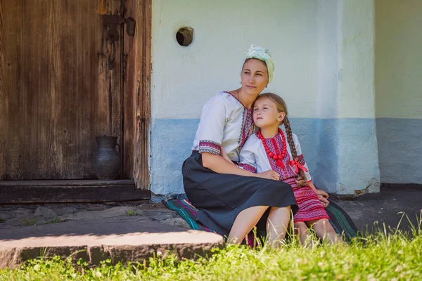 Μητέρα και κόρη στην ουκρανική εθνική κοστούμια κάθονται κοντά στο σπίτι — Φωτογραφία Αρχείου