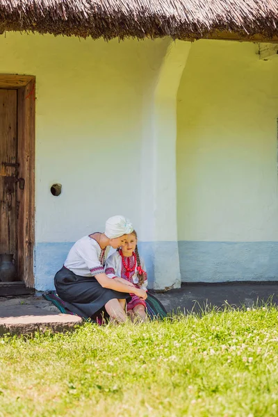 Mother and daughter in Ukrainian national costumes are sitting near the house — Stock Photo, Image