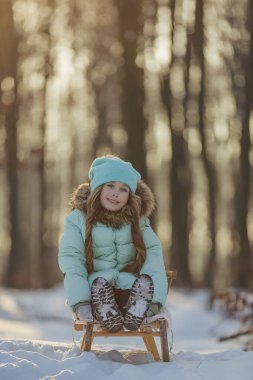 Küçük kız kızakta oturuyor.