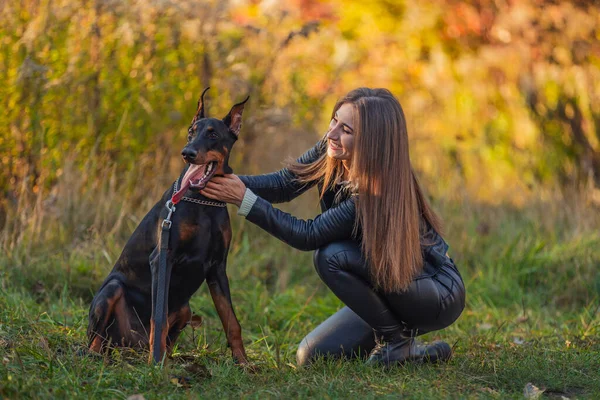 Kız bir doberman köpeğinin yanında oturuyor.