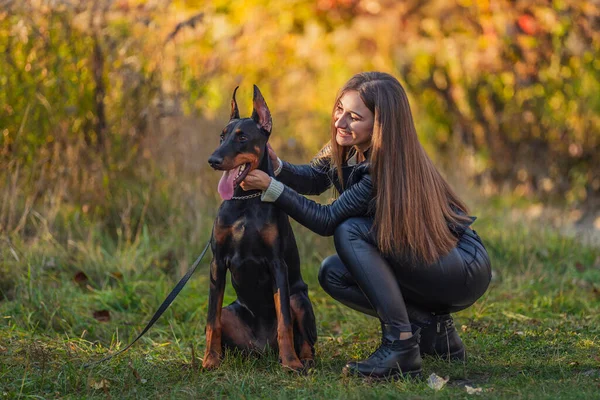 Kız bir doberman köpeğinin yanında oturuyor.