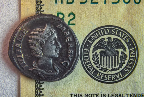 An old Roman coin lies on a 100 dollar bill — стоковое фото