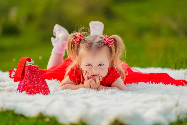 Girl in a red dress lies on a white blanket — Stockfoto