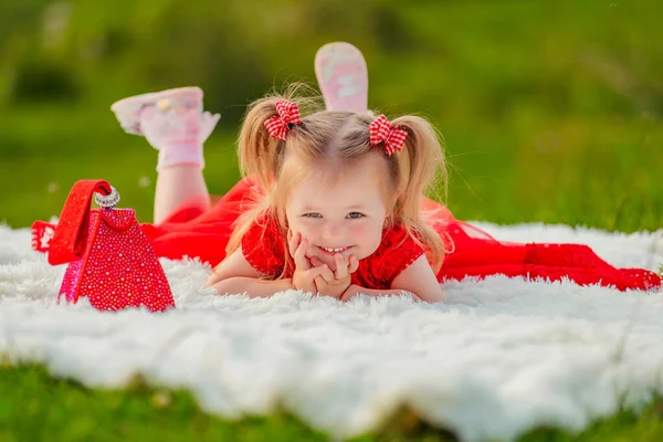 Girl in a red dress lies on a white blanket — Stock fotografie