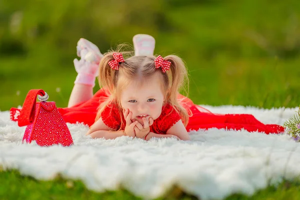 Girl in a red dress lies on a white blanket — Stockfoto