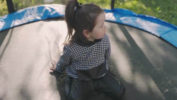 Lány nézi a telefont, miközben ül a trambulinon — Stock videók