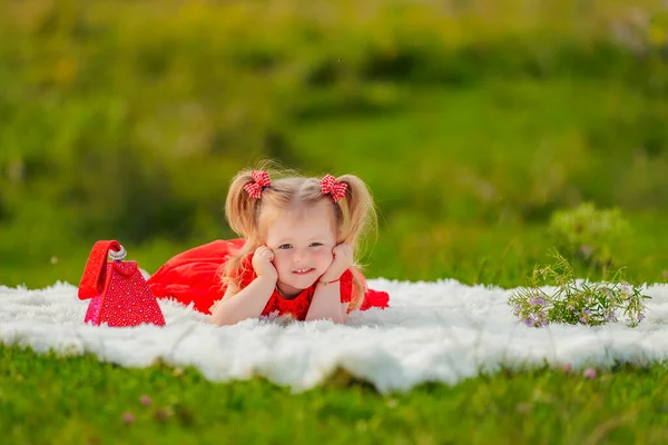 Menina em um vestido vermelho jaz em um cobertor branco — Fotografia de Stock