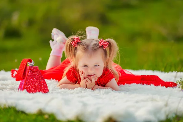 Girl in a red dress lies on a white blanket — Stockfoto