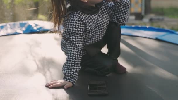 Little Girl Looking Phone While Sitting Trampoline — ストック動画