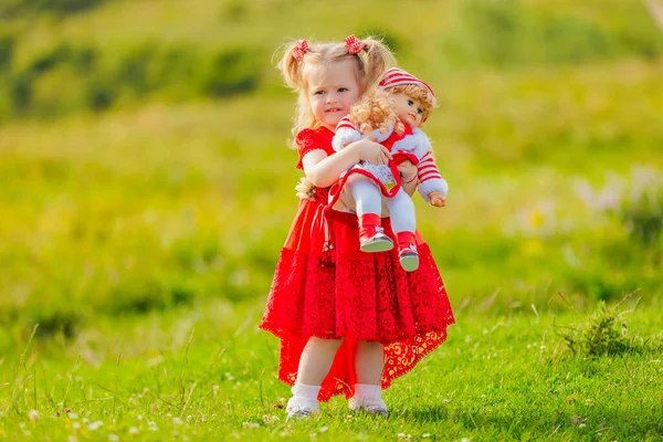 Kırmızı Elbiseli Bir Kız Elinde Oyuncak Bir Bebekle Doğada Duruyor — Stok fotoğraf