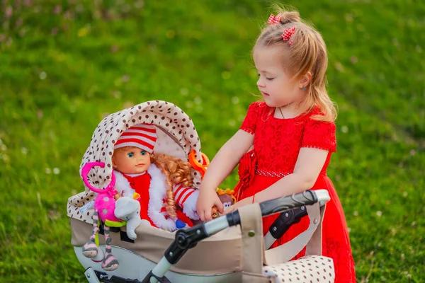 女の子はおもちゃのベビーカーに座っている彼女の人形と遊ぶ — ストック写真