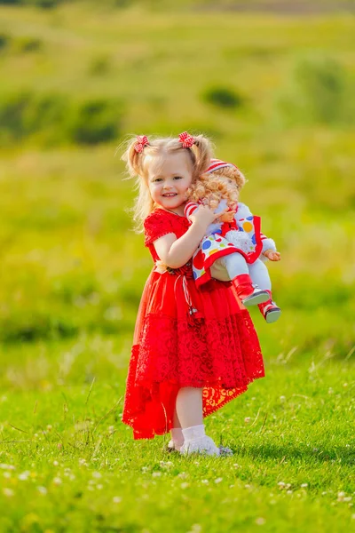 身着红色衣服 手里拿着洋娃娃的女孩站在大自然中 — 图库照片