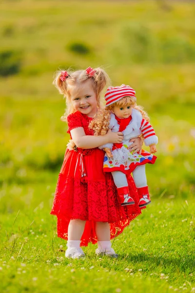 赤いドレスを着た女の子と手に人形が自然の中に立っていて — ストック写真