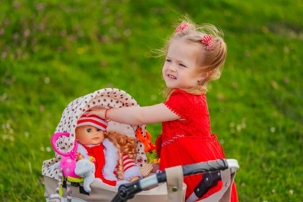 女の子はおもちゃのベビーカーに座っている彼女の人形と遊ぶ — ストック写真