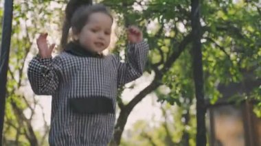 Kız bahçede trambolinde zıplıyor.