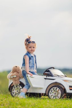 Küçük çocuk çimlerin üzerinde arabasının yanında duruyor.