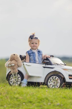 Küçük çocuk çimlerin üzerinde arabasının yanında duruyor.