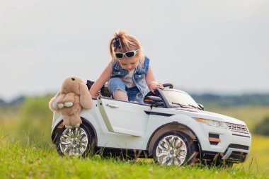 Küçük çocuk çimlerin üzerinde arabasının yanında duruyor.