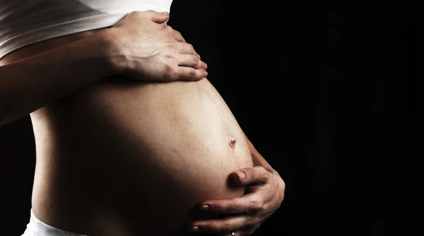 Pregnant belly with hands closeup on black background — Stock Photo, Image