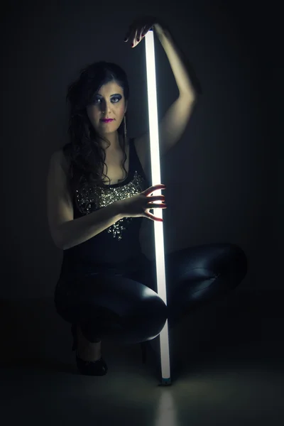 अंधेरे चमड़े के कपड़े में सुंदर लड़की एक प्रकाश ट्यूब पकड़े हुए — स्टॉक फ़ोटो, इमेज