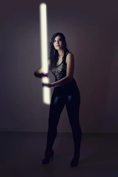 Hermosa chica en ropa de cuero oscuro sosteniendo un tubo de luz — Foto de Stock