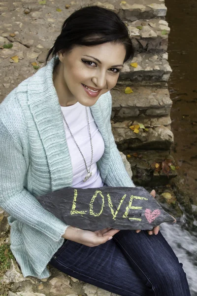 Gelukkig jonge vrouw toont de woorden, liefde, op een steen — Stockfoto