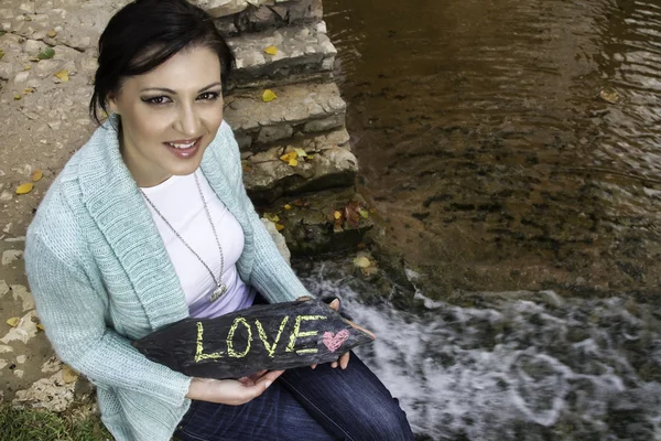 Gelukkig jonge vrouw toont de woorden, liefde, op een steen — Stockfoto