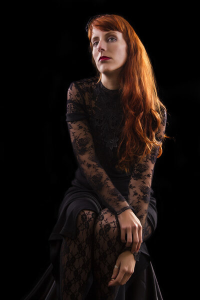 Beautiful girl on a black gothic dress with red hair isolated on a black background.
