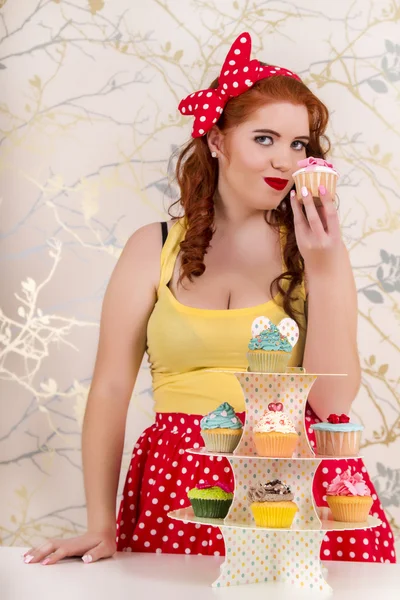 Mooie pinup roodharige meisje met kleurrijke cupcakes — Stockfoto