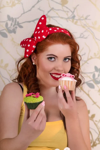 Mooie pinup roodharige meisje houdt van een kleurrijke cupcakes — Stockfoto