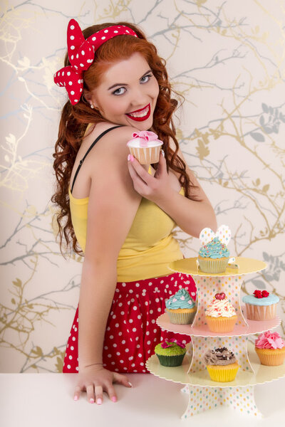 Beautiful pinup redhead girl holding a colorful cupcake