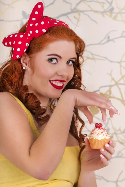 Hermosa chica pelirroja pinup sosteniendo un cupcake colorido — Foto de Stock