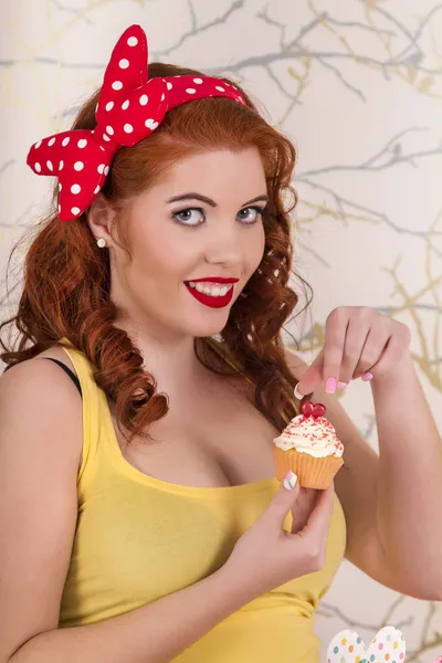 Mooie pinup roodharige meisje houdt van een kleurrijke cupcake — Stockfoto