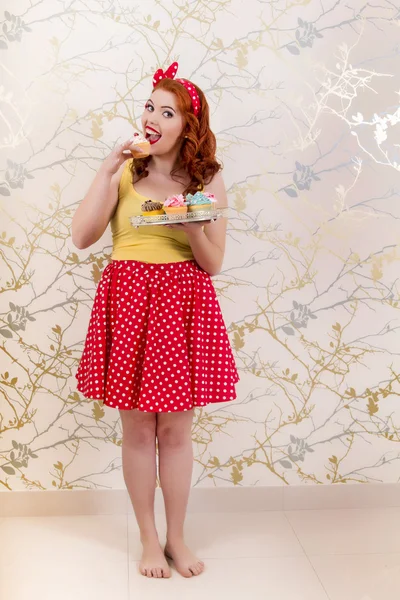 Hermosa chica pelirroja pinup sosteniendo una bandeja de cupcakes de colores — Foto de Stock