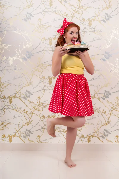 Belle fille rousse pinup tenant un plateau de cupcakes colorés — Photo