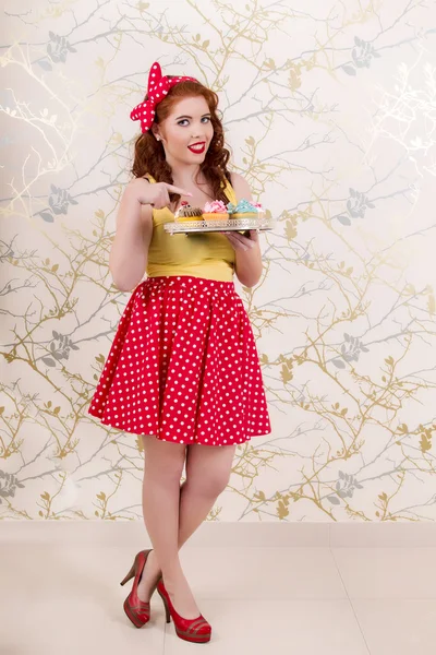 Bella pinup rossa ragazza che tiene un vassoio di cupcake colorati — Foto Stock